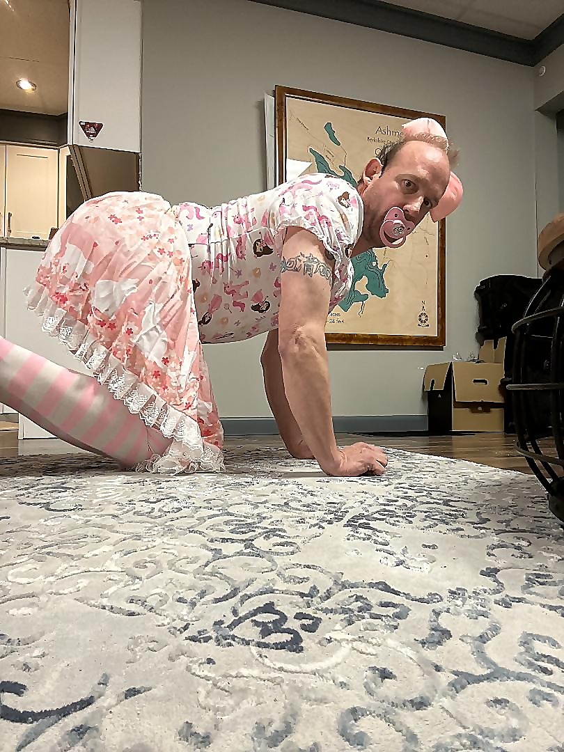 Jessica kneeling on a rug in a pink floral ruffled outfit, striped stockings and a pink pacifier